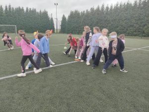 Grupa uczniów uczestniczy w zabawie ruchowej z piłką na szkolnym boisku.