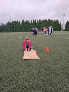Uczennica przygotowuje się do kolejnego etapu wyścigu w workach, a pozostali uczniowie czekają na swoją kolej.