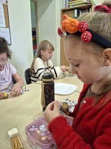 Uczennice przy stoliku przygotowują ziemniaki podczas zajęć związanych ze Świętem Pieczonego Ziemniaka.