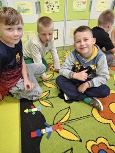 Uczniowie klasy I podczas zajęć matematycznych na dywanie prezentują ułożone z figur geometrycznych kompozycje.