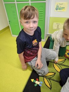 Uczeń klasy I podczas zajęć na dywanie układa kompozycję z kolorowych figur geometrycznych.
