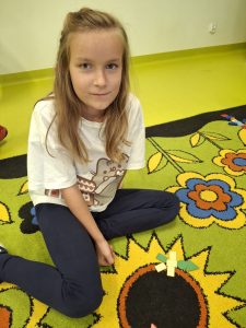 Uczennica klasy I prezentuje kompozycję ułożoną z figur geometrycznych podczas zajęć matematycznych.