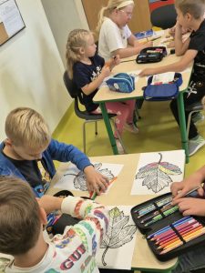 Grupa dzieci w świetlicy szkolnej przygotowuje kolorowe prace plastyczne przedstawiające jesienne liście.