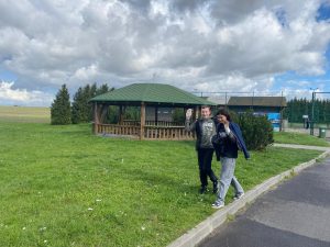 Dwoje uczniów z workiem na odpady idzie wzdłuż trawnika obok szkolnej altany.