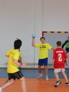 Uczeń w żółtej koszulce przygotowuje się do rzutu piłką podczas meczu piłki ręcznej.