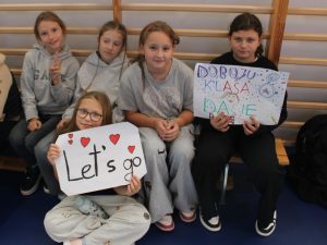 Grupa uczennic kibicujących podczas zawodów prezentuje plakaty z hasłami „Let's go” i „Do boju klasa 8, dacie radę”.