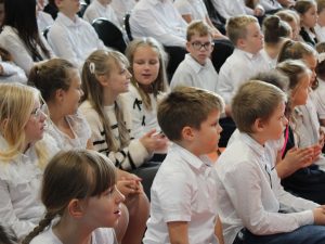 Uczniowie siedzący na widowni podczas akademii. Część dzieci klaszcze, a pozostali obserwują występ.