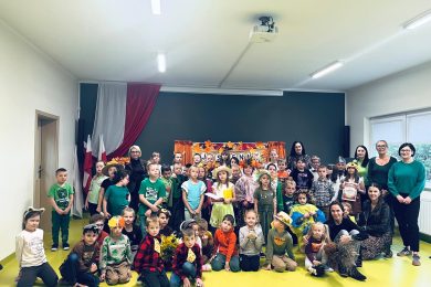 Uczniowie klas 0–III wraz z nauczycielami pozują do wspólnego zdjęcia po jesiennym koncercie. Dzieci mają na sobie kolorowe stroje i przebrania związane z jesienią.