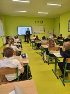Psycholog szkolna prowadzi zajęcia dla uczniów klasy I, wyjaśniając swoją rolę i zadania przy wykorzystaniu prezentacji na ekranie interaktywnym.