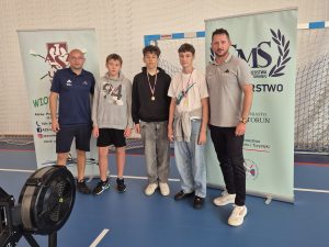 Trzech wyróżnionych uczniów z medalami po zakończeniu rywalizacji na ergometrach, w towarzystwie trenerów sekcji wioślarskiej.